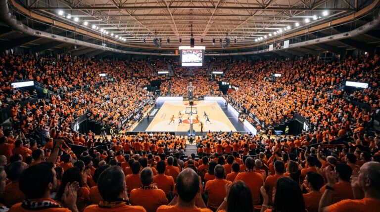 Pabellón de baloncesto lleno de aficionados vestidos de naranja durante un partido.